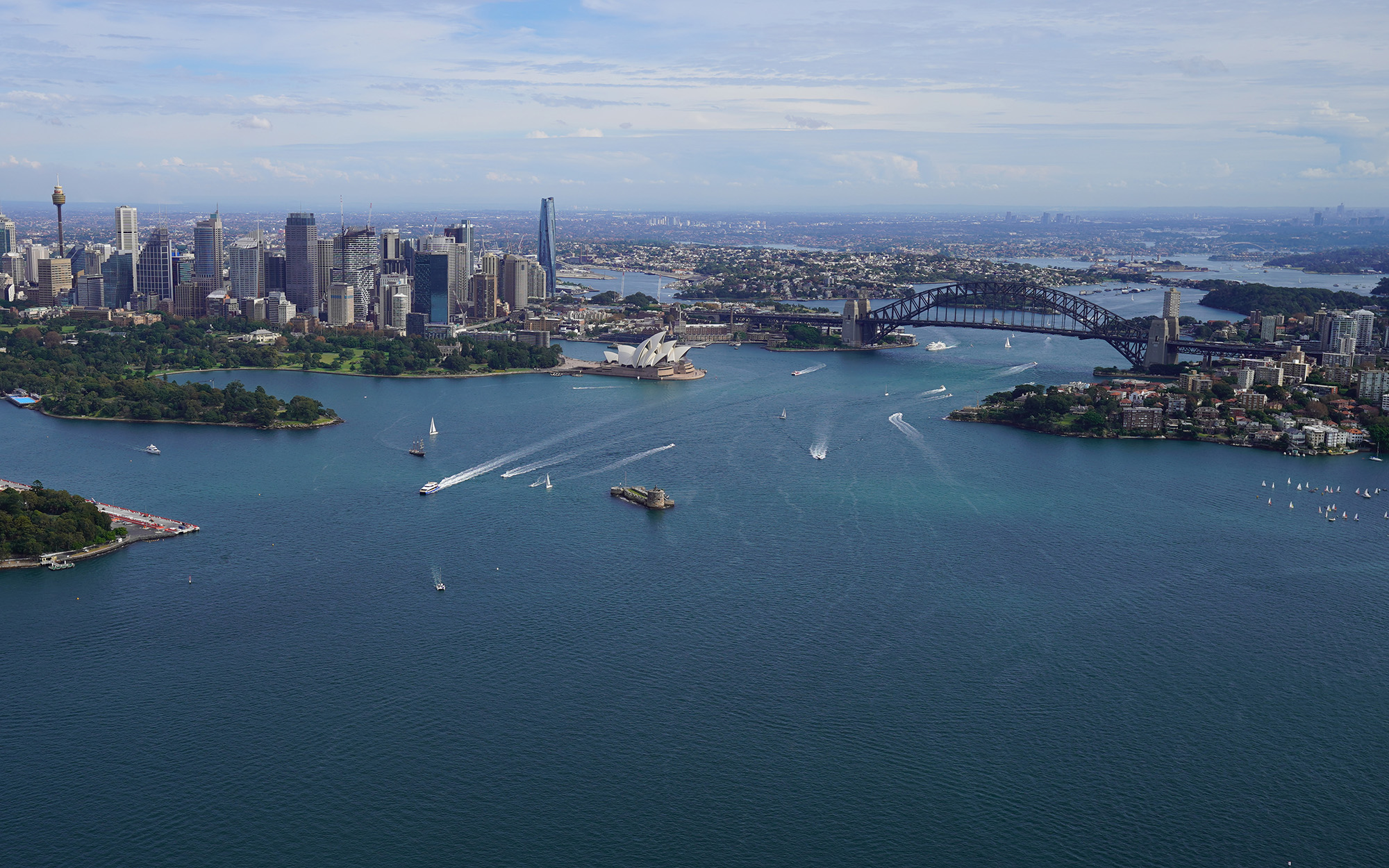 Elevated aerial view over Sydney Harbour from across Mosman and lower north shore suburbs towards city CBD landmarks and waterfront.