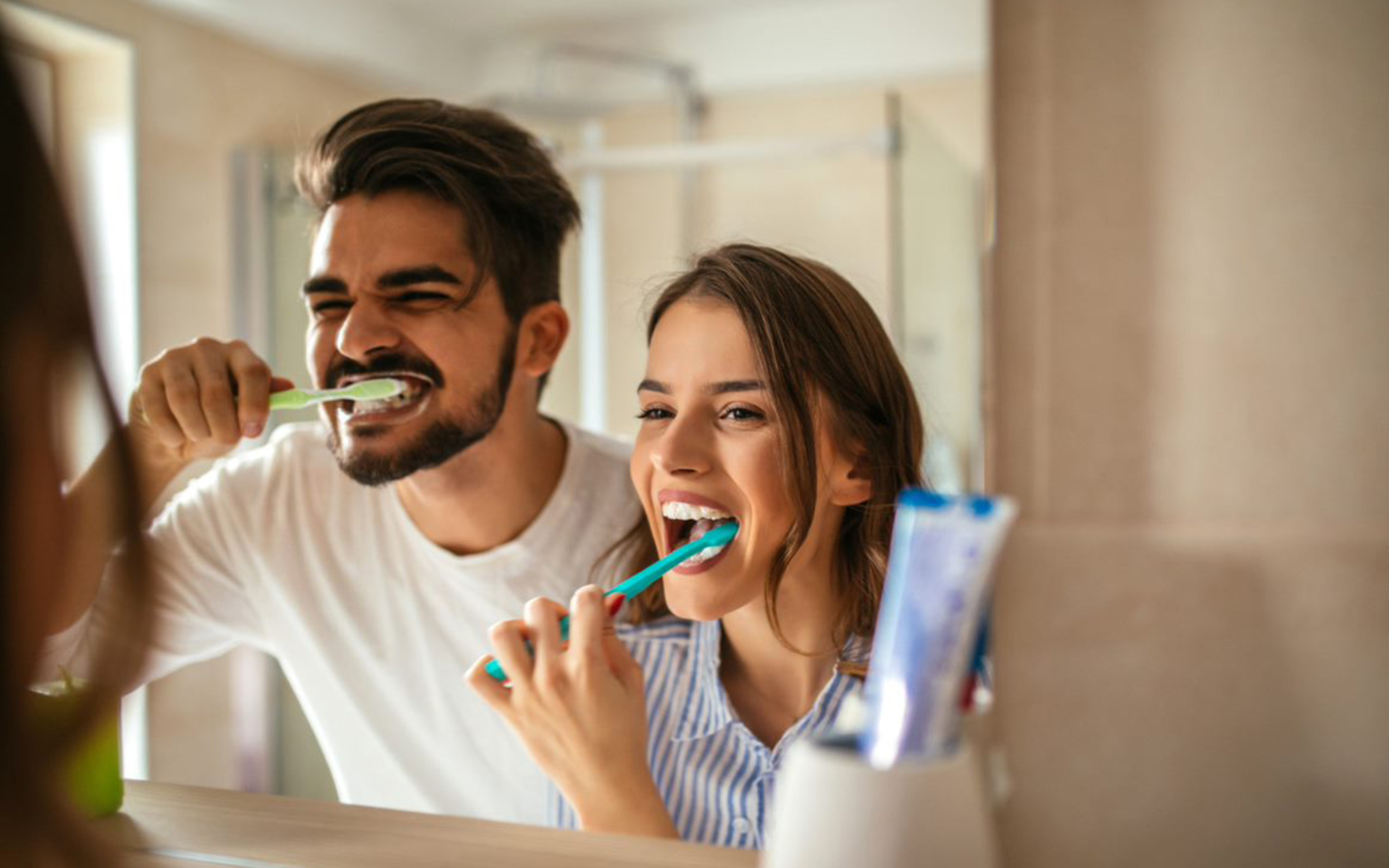 A man and a woman brushing their teeth in the mirror