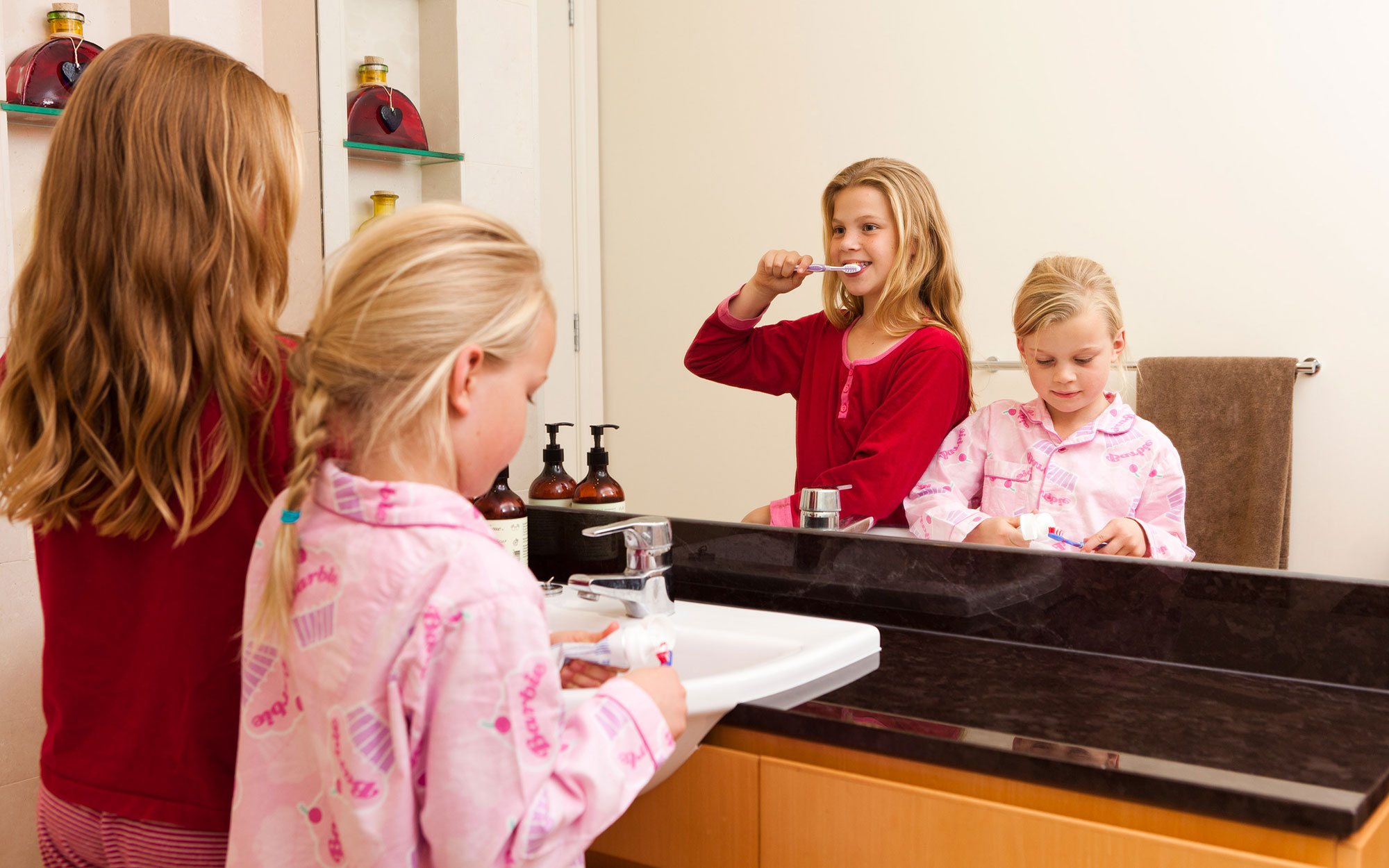 Two young girls wearing pink and brushing teeth in the mirror
