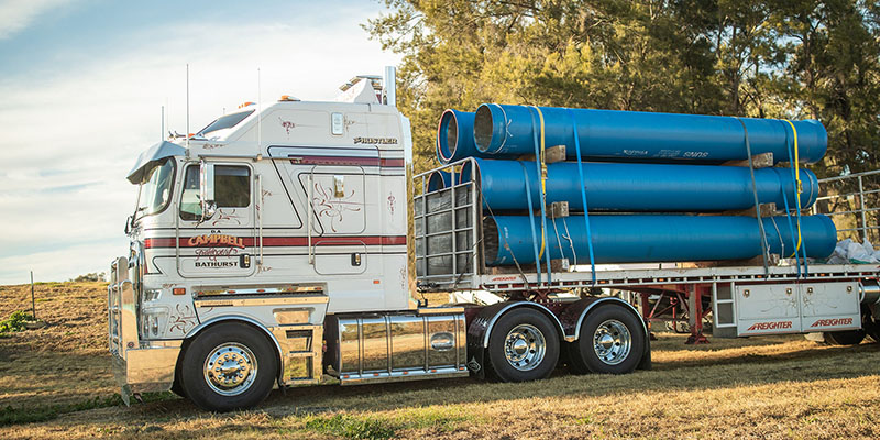 Truck carrying large blue pipes