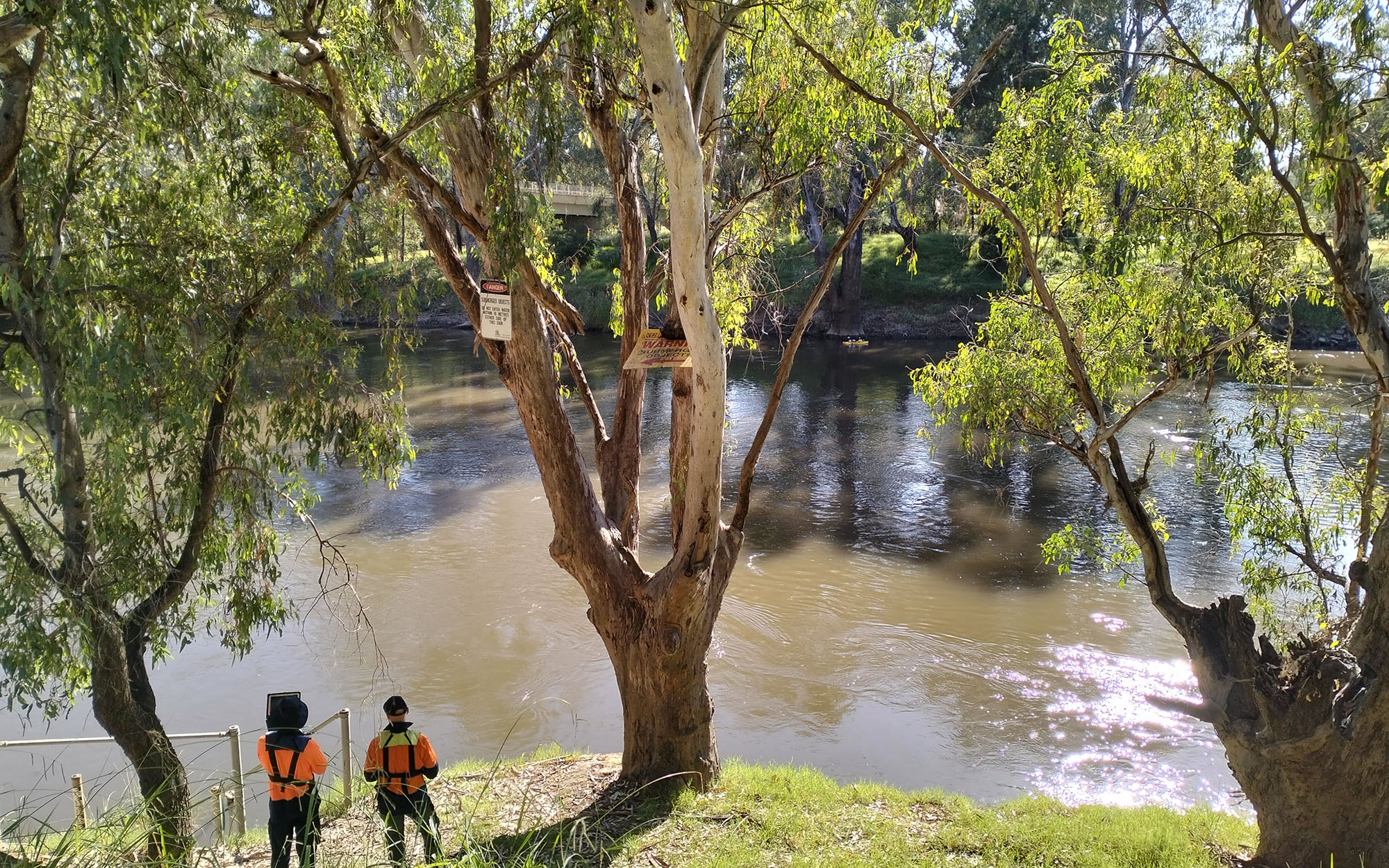 Two men in high vis watching the river with gum trees. Image credit: Siv Teh DPE 