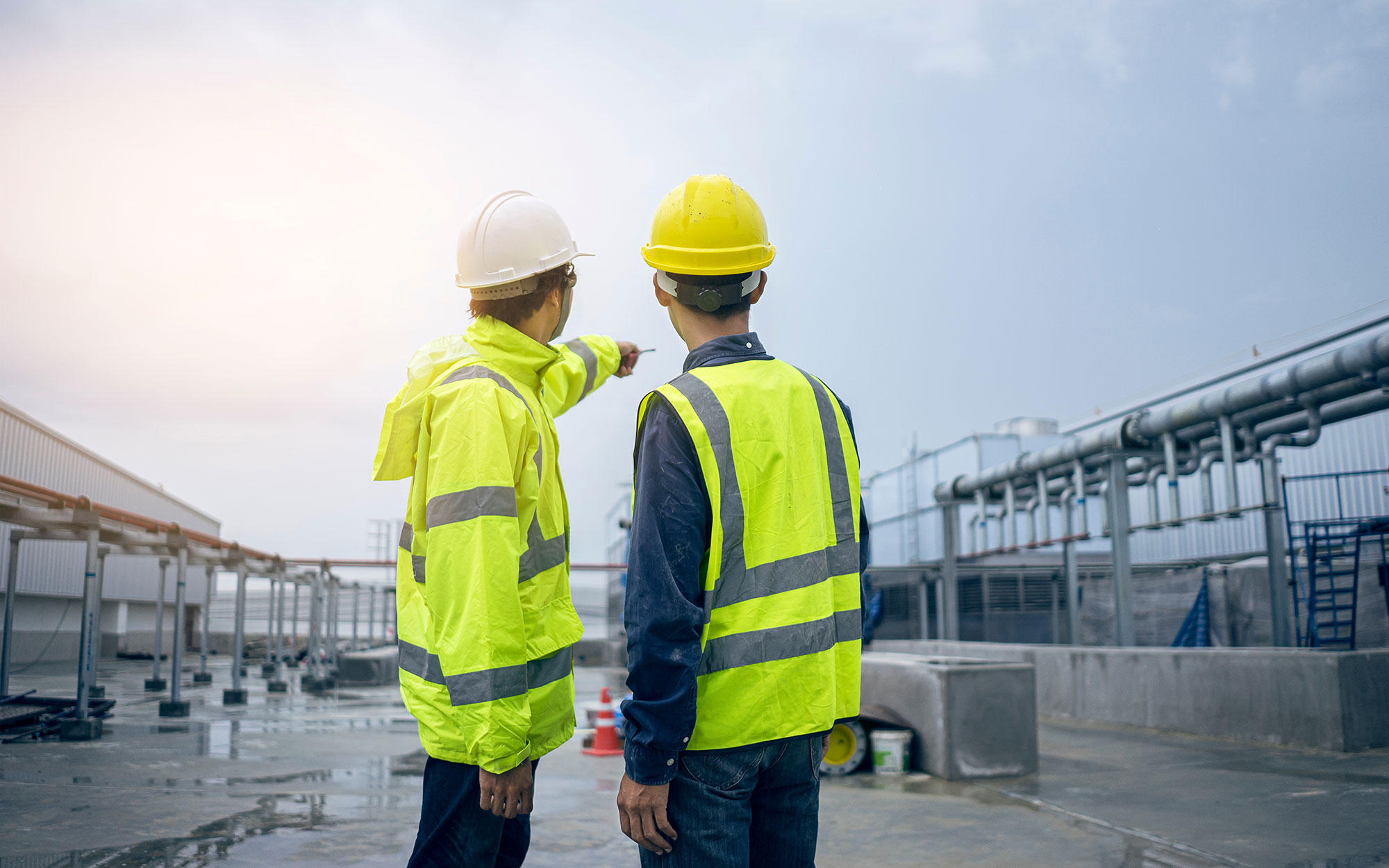 Two people in high vis clothing pointing at a pipes on a construction site